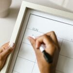 Osoba zaznacza termin wydarzenia markerem w papierowym kalendarzu