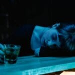 Zmęczona kobieta z drinkiem opiera głowę o stolik w ciemnym klubie