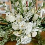 Biała kompozycja kwiatowa z zielenią jako dekoracja weselnego stołu