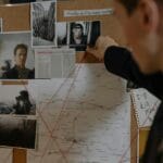 Detektyw analizuje tablicę z dowodami podczas śledztwa w sprawie morderstwa