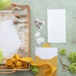 Papeteria ślubna na pastelowym tle z kopertami i zielonymi kwiatami