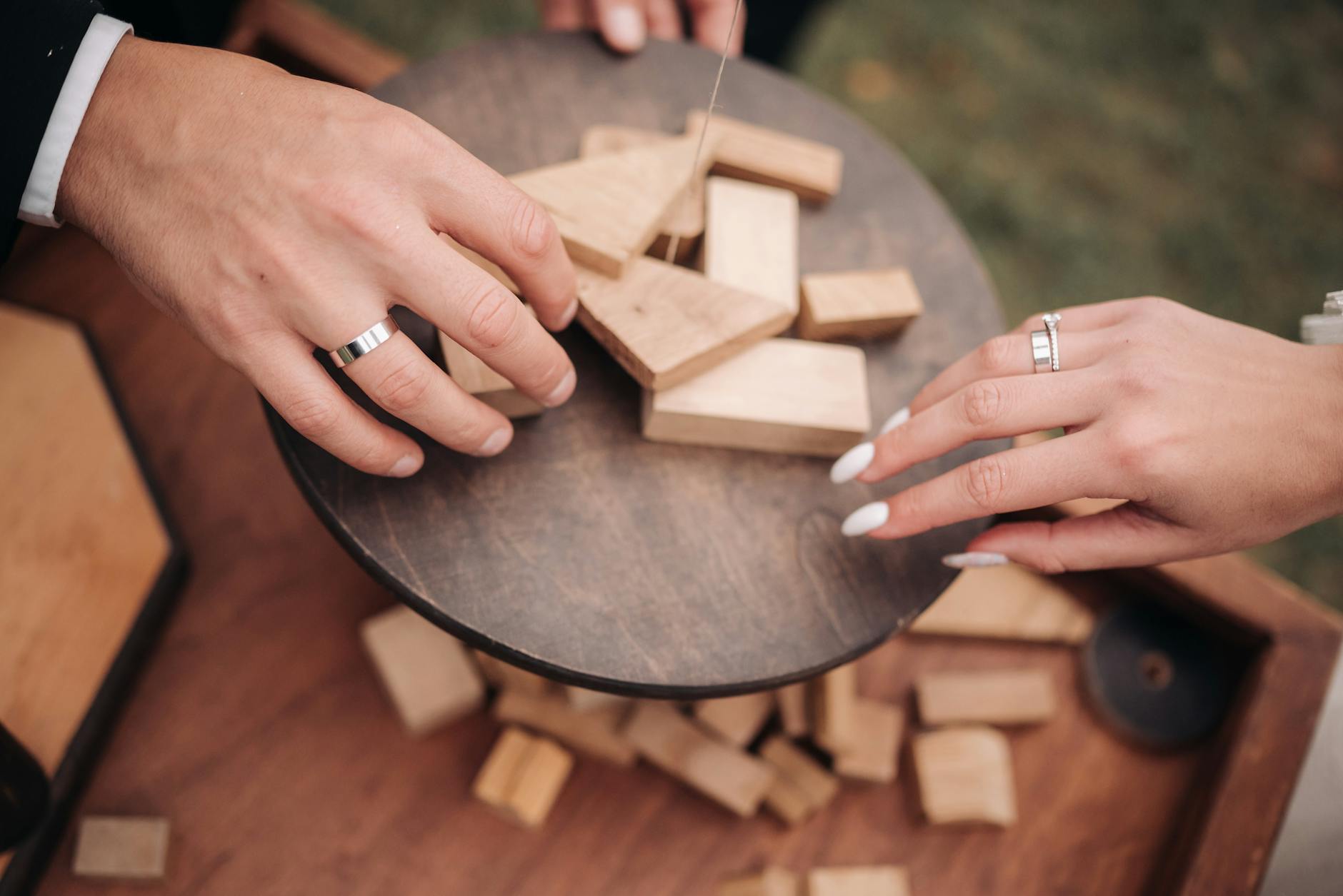Dłonie układające drewniane klocki z obrączkami na weselnym stole